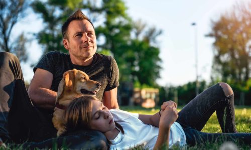 Father and daughter relaxing at park with small yellow dog